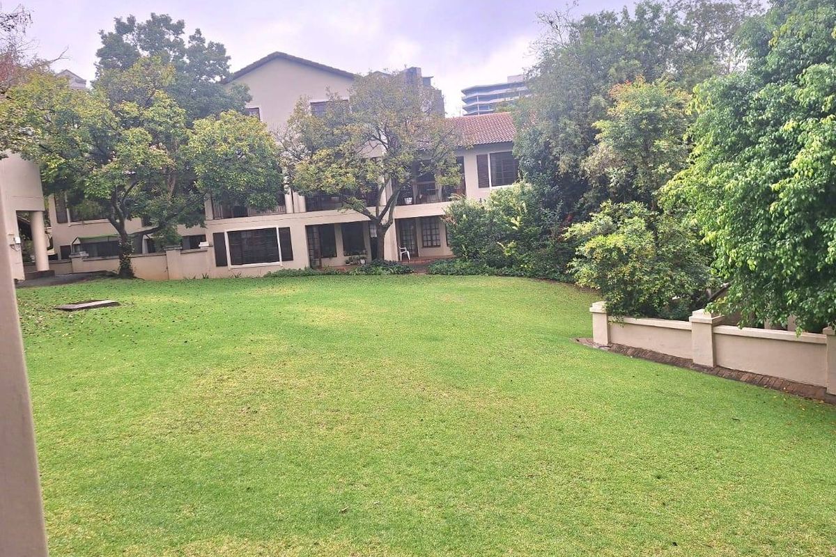 A view of the rear exterior of the apartment complex, featuring a large, well-maintained lawn and mature trees.