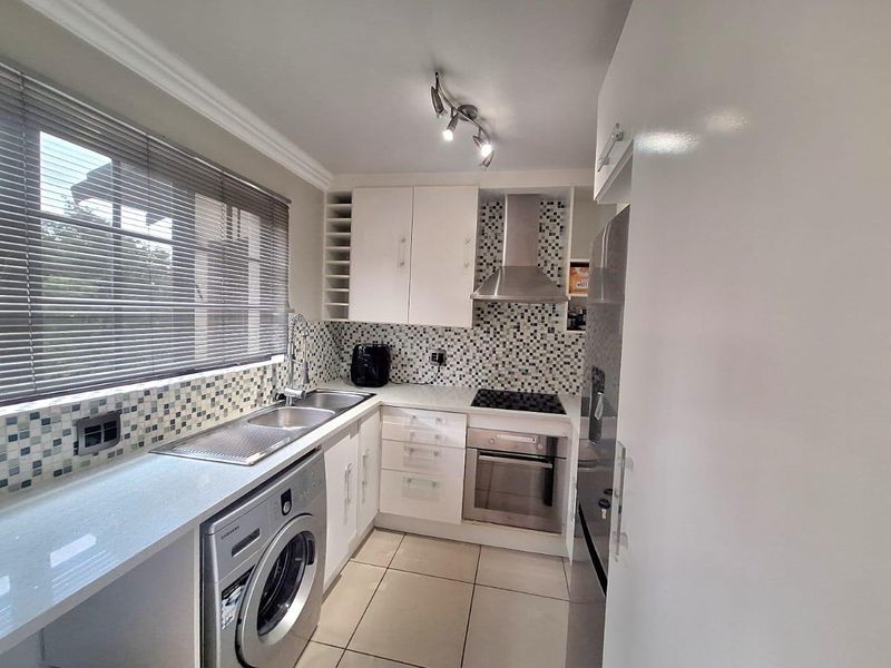 A well-maintained kitchen featuring modern white cabinetry, stone countertops, mosaic tile backsplash, and integrated stainless steel appliances including an oven and hob.