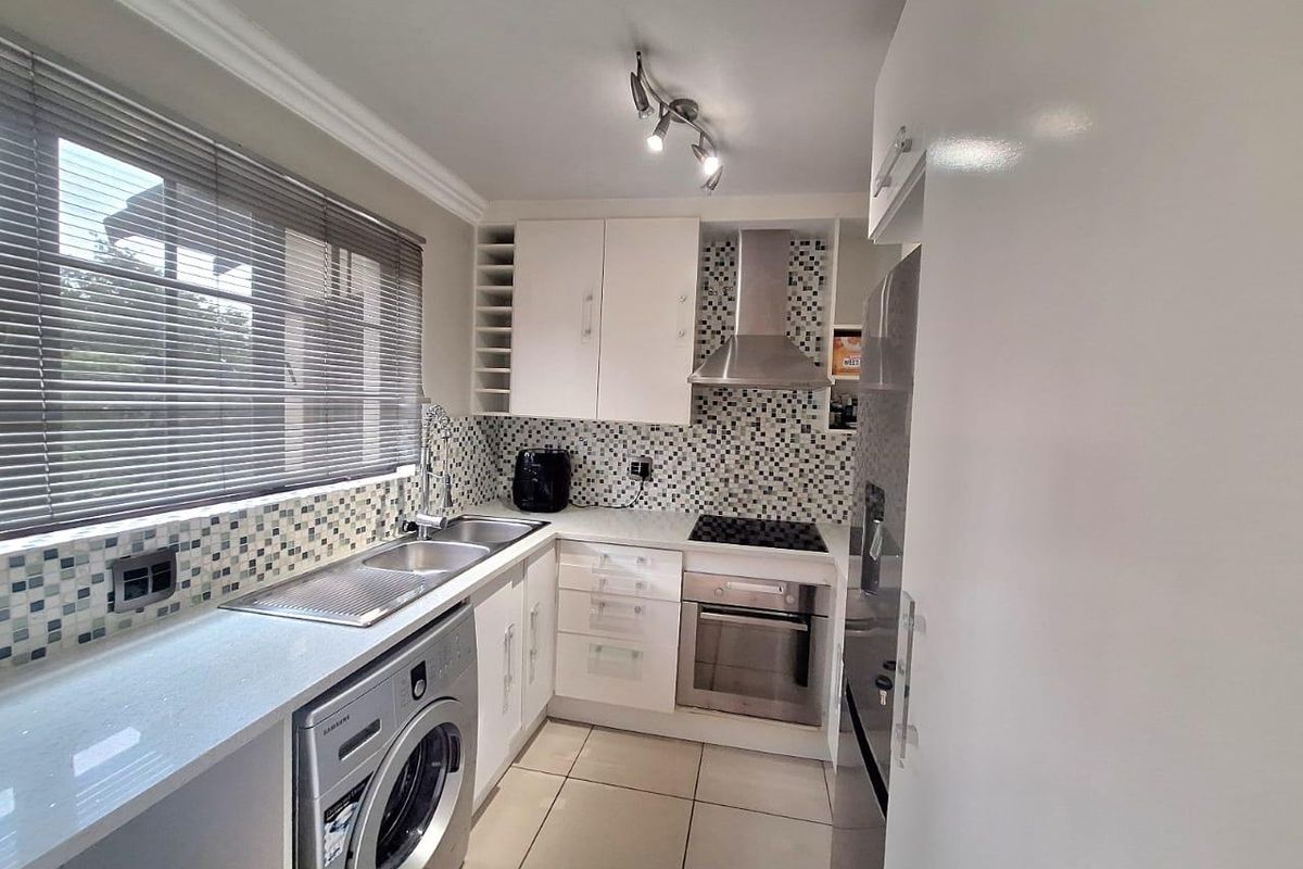 A well-maintained kitchen featuring modern white cabinetry, stone countertops, mosaic tile backsplash, and integrated stainless steel appliances including an oven and hob.