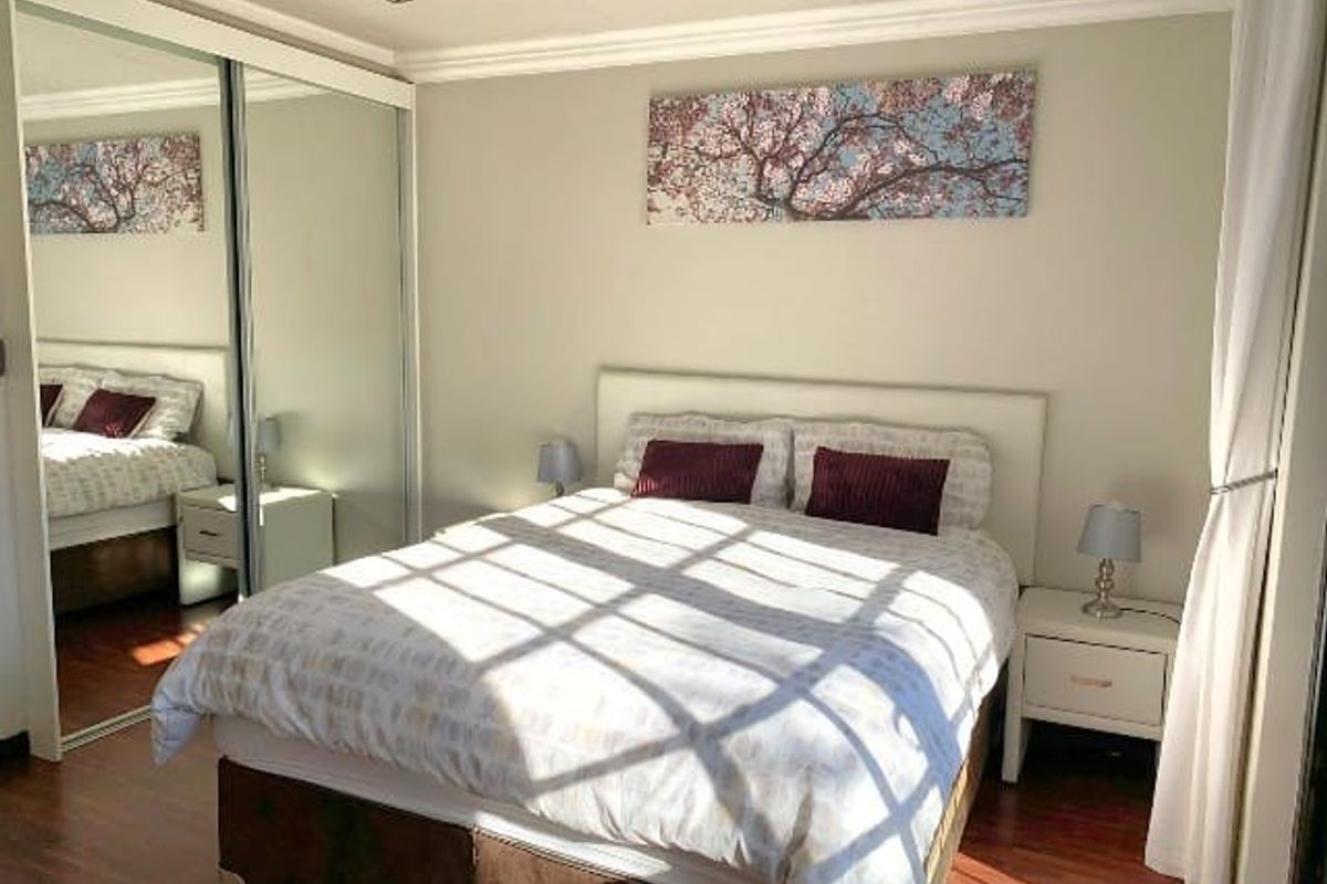 A well-maintained bedroom featuring laminate flooring, recessed ceiling lighting, and large mirrored sliding wardrobe doors that enhance the sense of space.