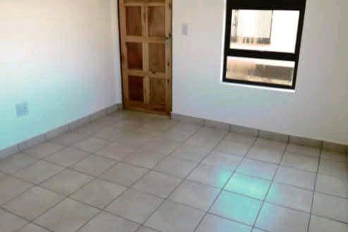 An empty bedroom featuring neutral tiled flooring, a timber door, and an aluminium-framed window, providing a clean canvas for interior design.