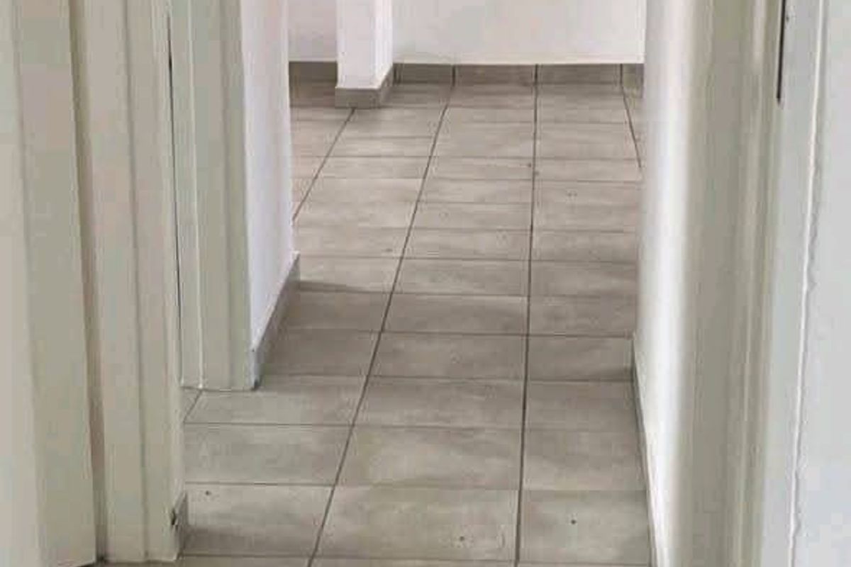 A vacant hallway featuring neutral grey floor tiles and white walls, providing a clean and simple transition space between rooms.