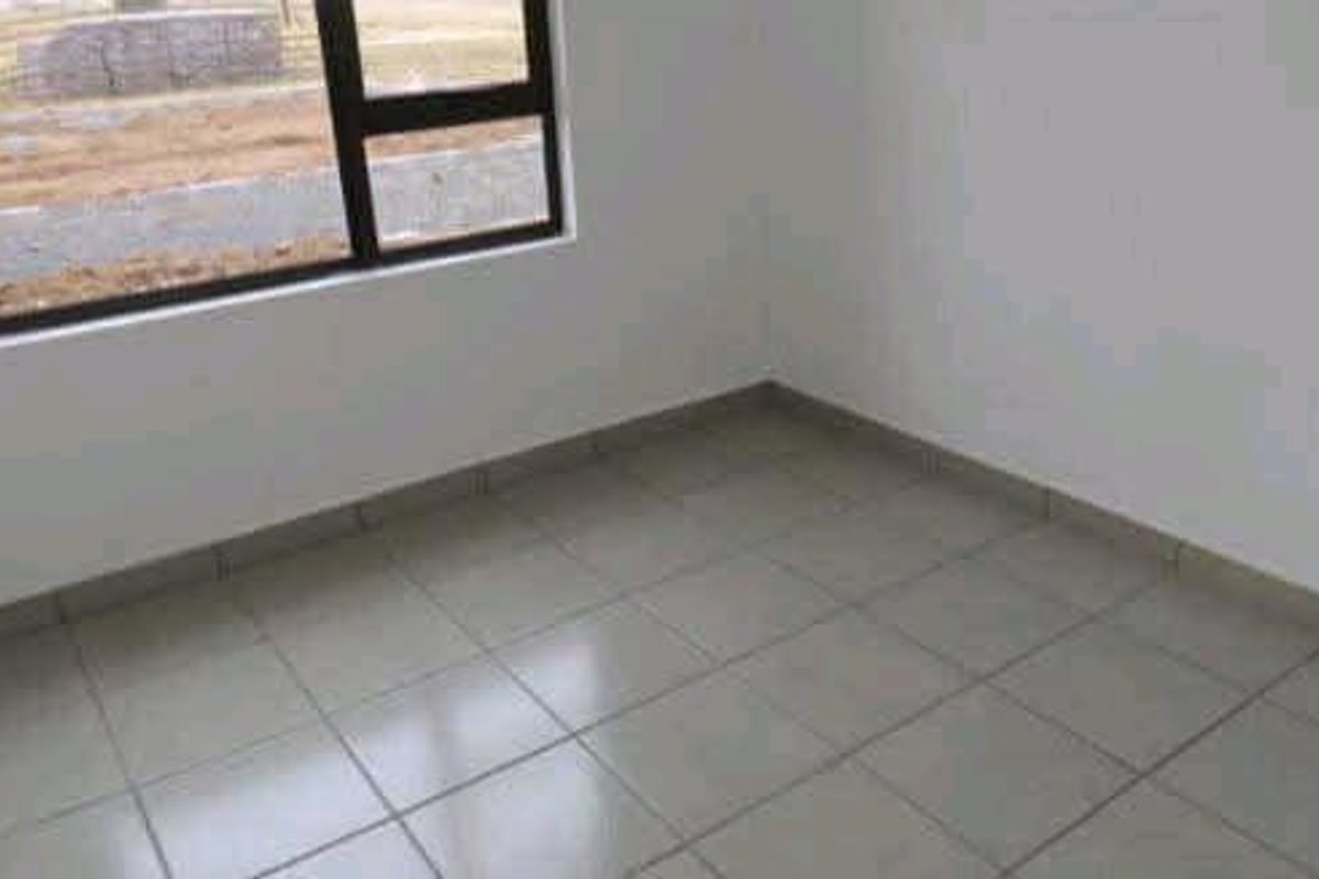 A clean, empty bedroom featuring neutral tiled flooring, white walls, and a modern aluminium-framed window.