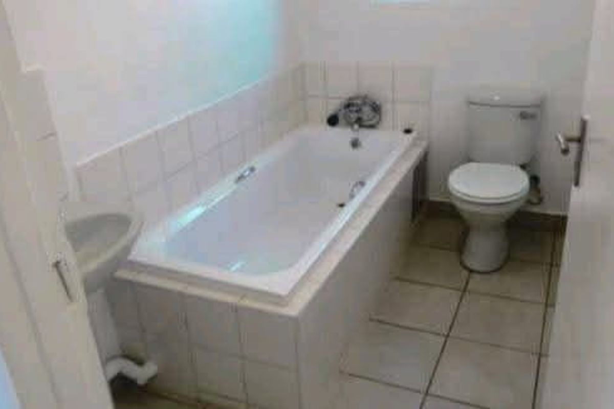 A functional bathroom featuring a built-in bathtub, wall-mounted basin, and toilet with neutral tiled flooring and splashbacks.