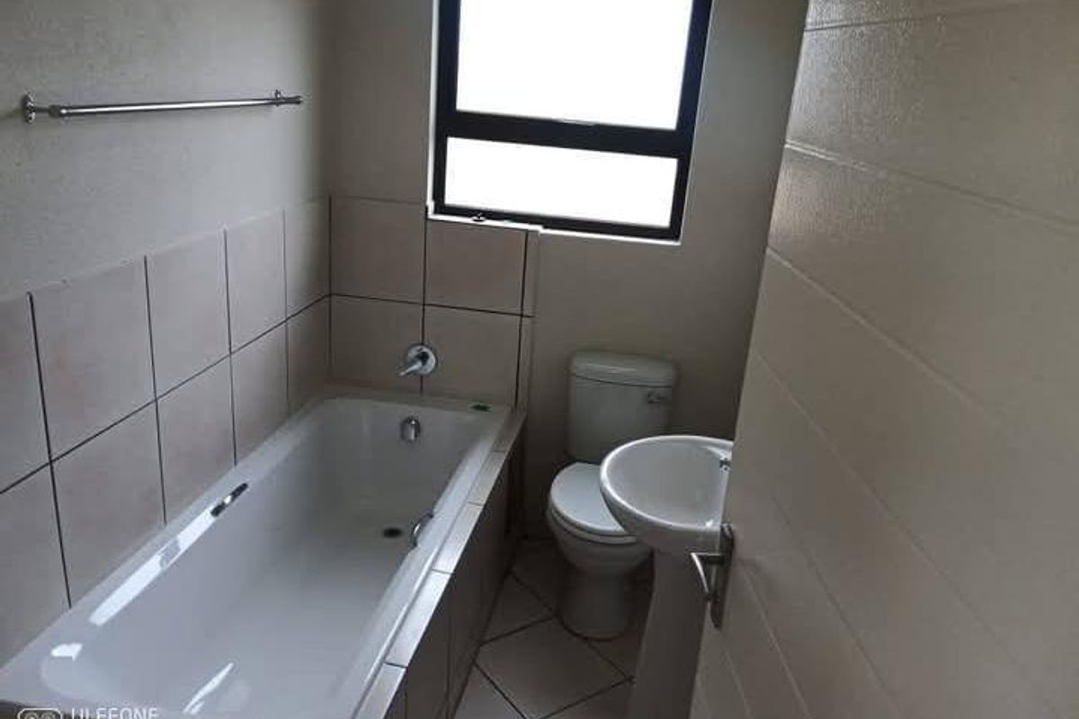 A functional bathroom featuring a standard bathtub, pedestal basin, and toilet with neutral wall and floor tiling.
