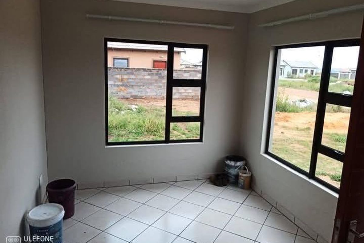 An empty living room featuring tiled flooring and large aluminium-framed windows, offering a bright and neutral space ready for personalization.