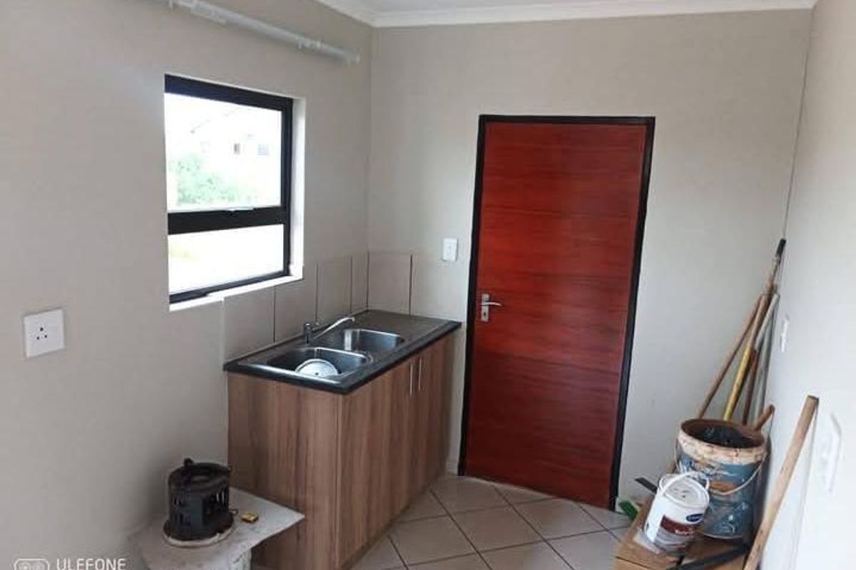A functional scullery or utility area featuring a double bowl sink, laminate cabinetry, tiled splashback, and tiled flooring with a solid timber door.