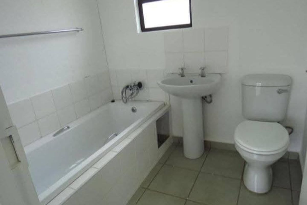 A functional bathroom featuring a pedestal basin, toilet, and built-in bathtub with tiled splashbacks and flooring.