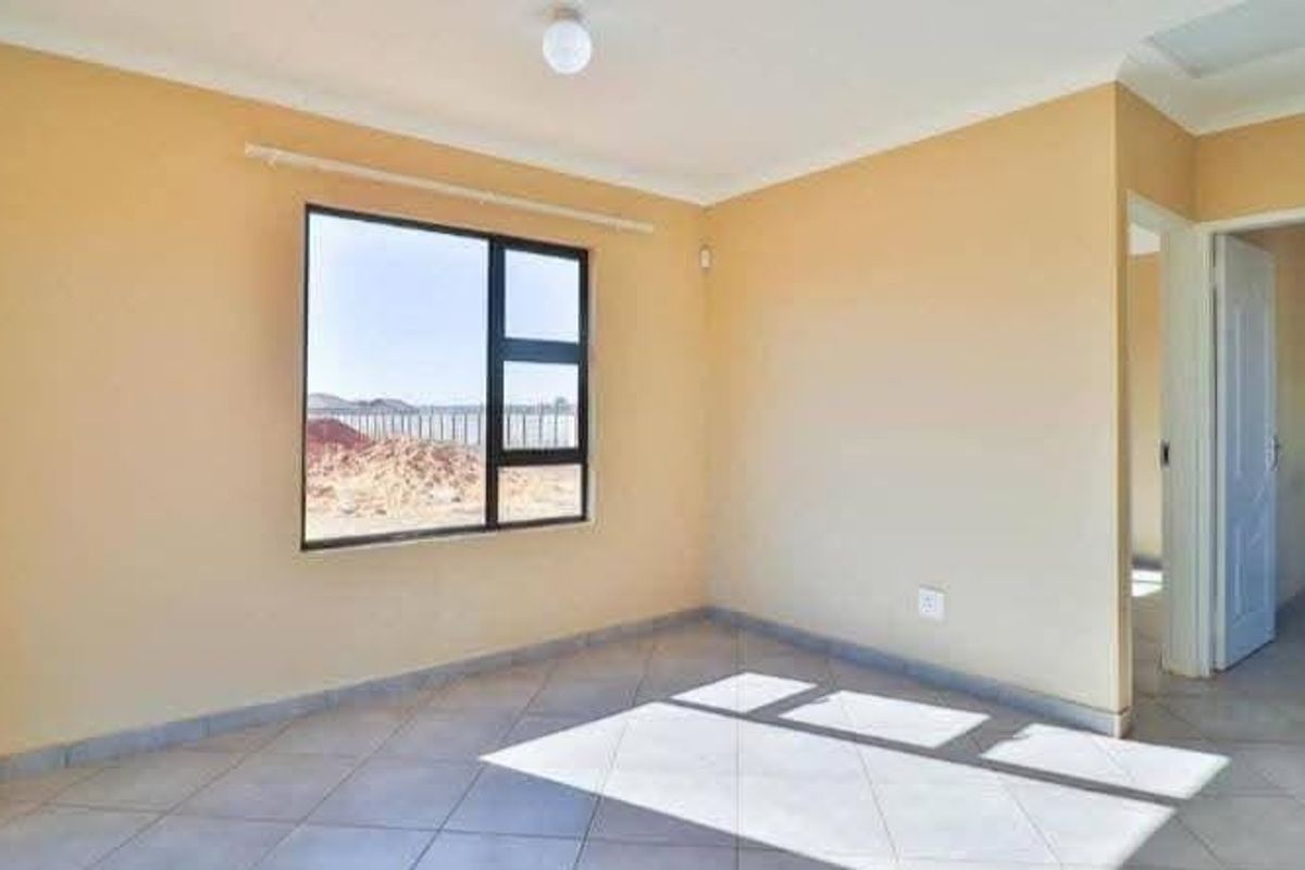 A bright, empty bedroom featuring neutral walls, tiled flooring, and an aluminium-framed window with natural light.