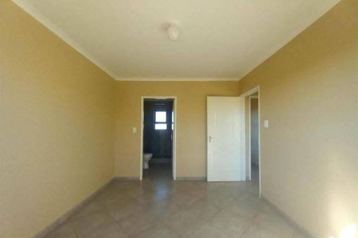An empty bedroom featuring neutral wall paint, tiled flooring, and coved ceilings, with direct access to an adjoining bathroom.
