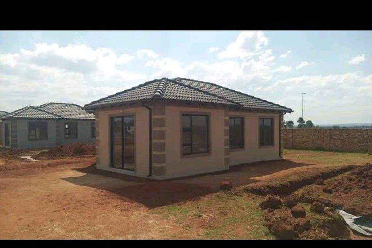 Rear view of a newly constructed house featuring a tiled roof, aluminium window frames, and a sliding glass door, set on an unlandscaped plot.