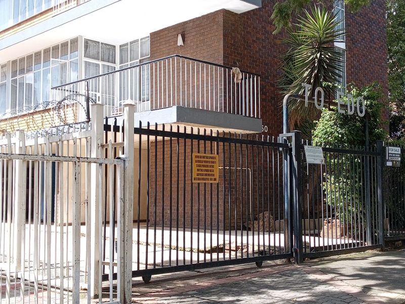 Front exterior view of a multi-story brick apartment building featuring balconies, secure gated access, and paved driveway area.