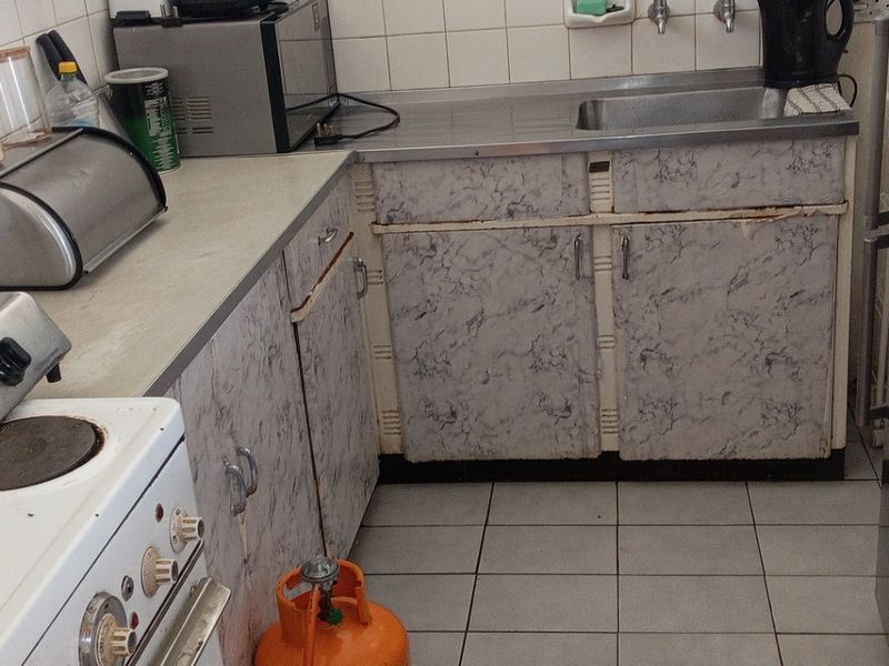 A compact kitchen featuring tiled flooring, a stainless steel sink, and dated laminate cabinetry in need of refurbishment.