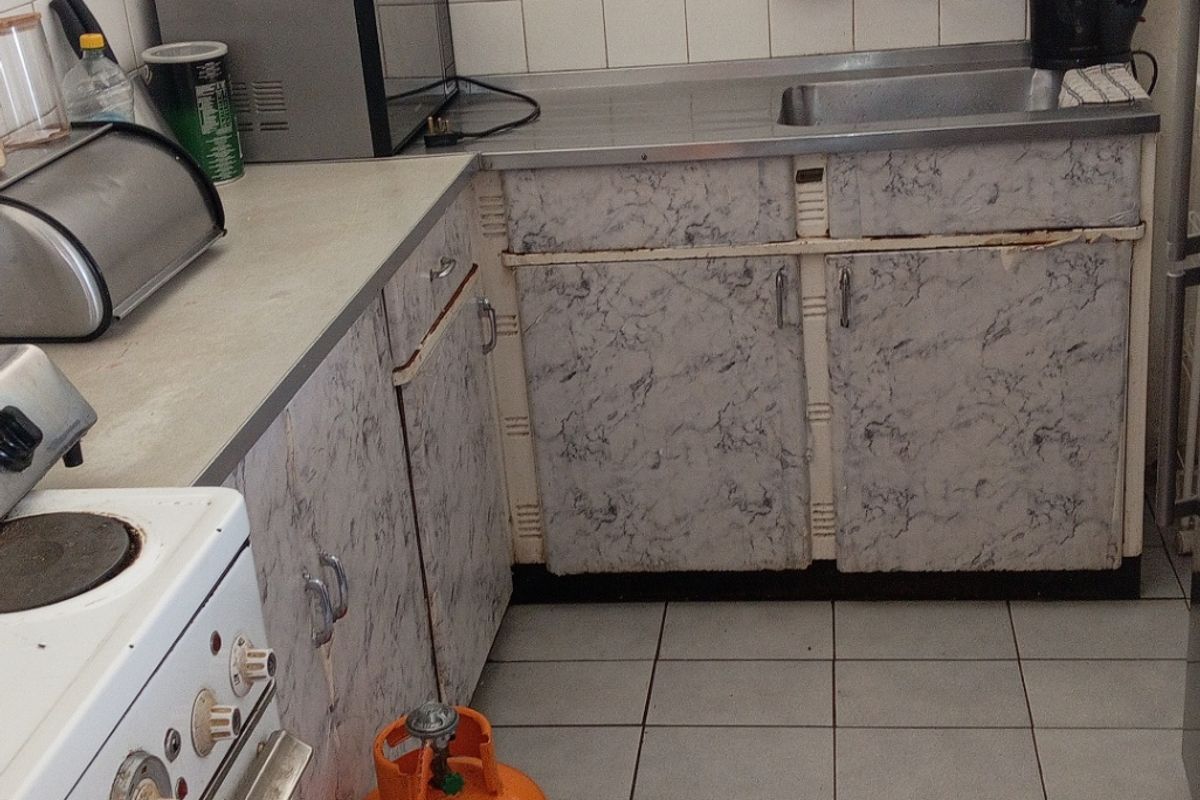 A compact kitchen featuring tiled flooring, a stainless steel sink, and dated laminate cabinetry in need of refurbishment.