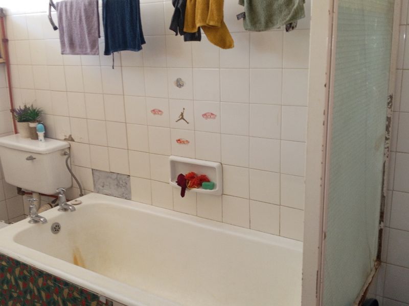 A dated bathroom featuring a bathtub, toilet, and tiled walls. The space requires renovation to update the finishes and address visible wear.