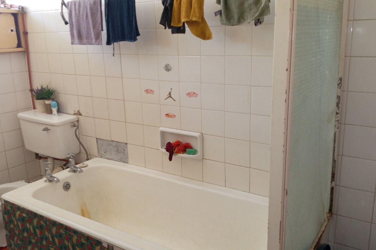 A dated bathroom featuring a bathtub, toilet, and tiled walls. The space requires renovation to update the finishes and address visible wear.