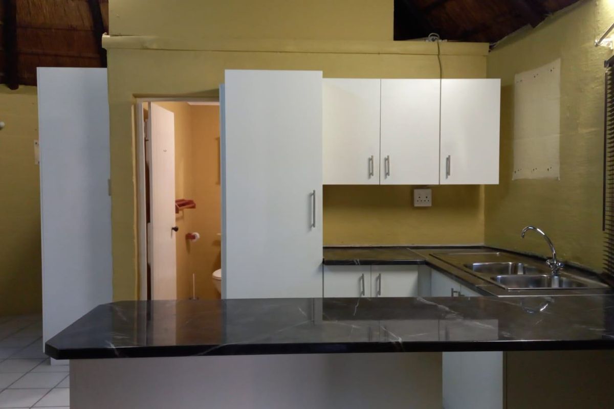 A functional kitchen area featuring dark laminate countertops, built-in white cabinetry, and a stainless steel sink, set under a traditional thatched roof.
