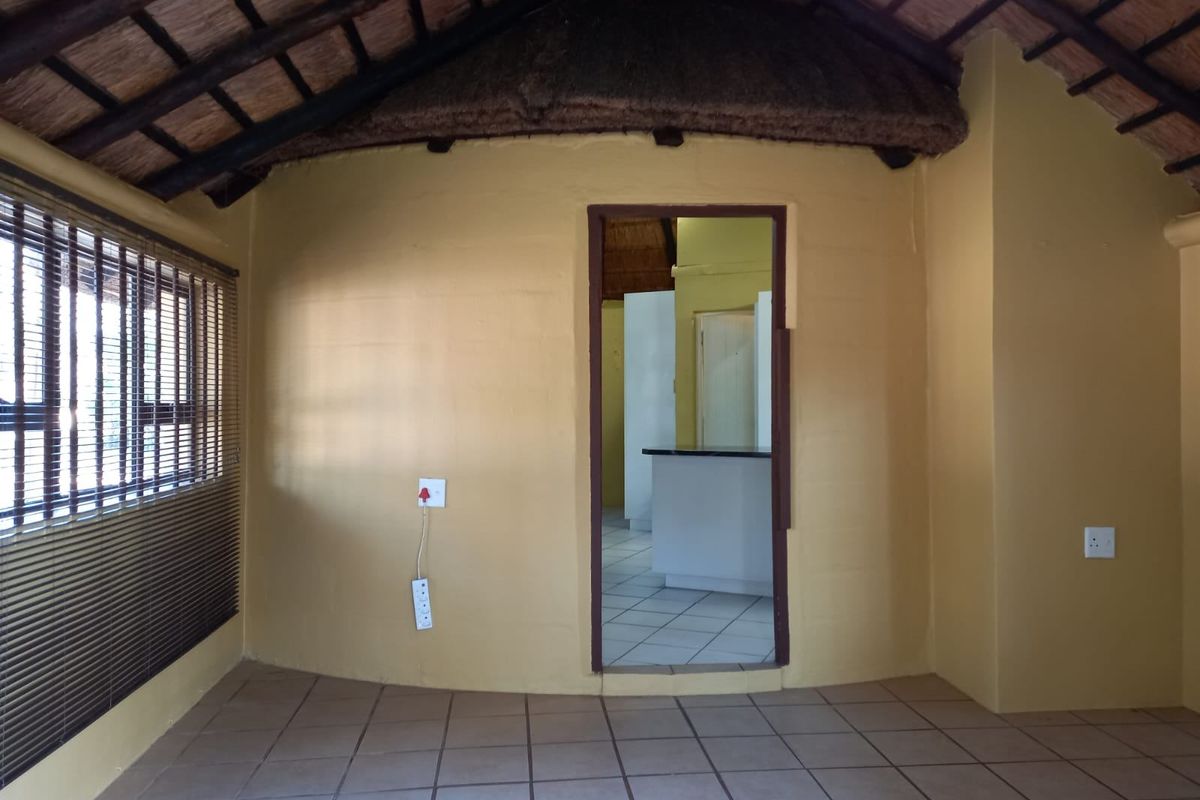 An empty living area featuring a traditional thatched roof with exposed rafters, ceramic tiled flooring, and a doorway leading to an adjacent space.