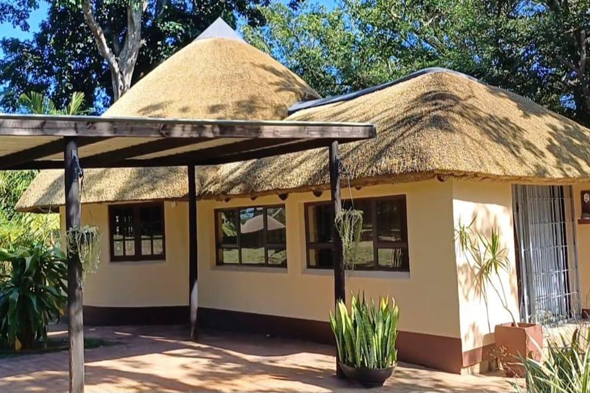 A charming cottage featuring a traditional thatched roof and a covered patio area, set within a lush, green garden environment.
