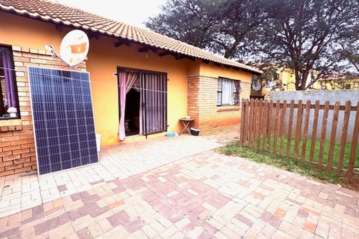 Rear exterior view of the townhouse featuring a paved patio area, brick facade, and a private fenced garden space.