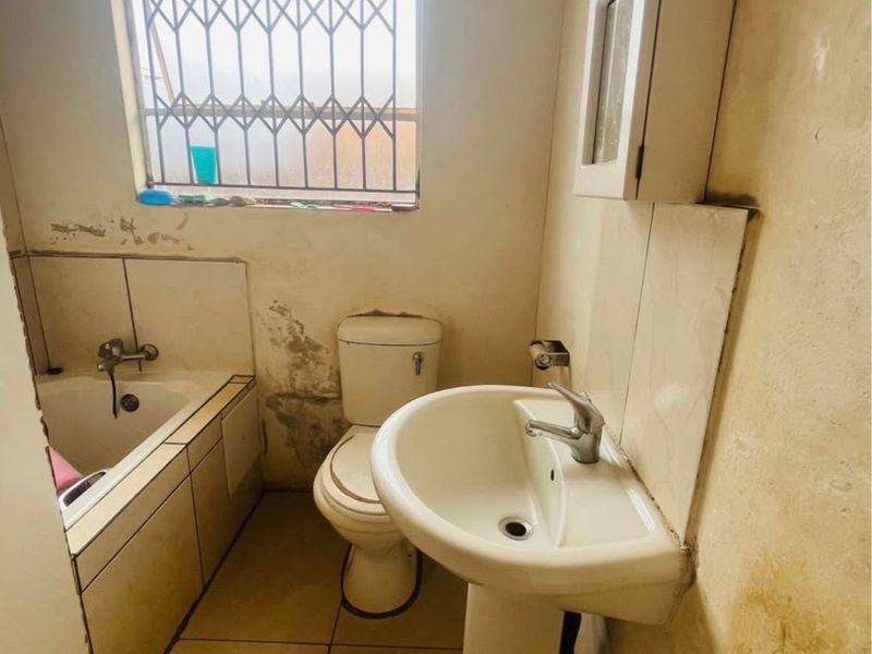 A dated bathroom featuring a bathtub, pedestal basin, and toilet, requiring significant cosmetic renovation and wall repairs to restore its condition.