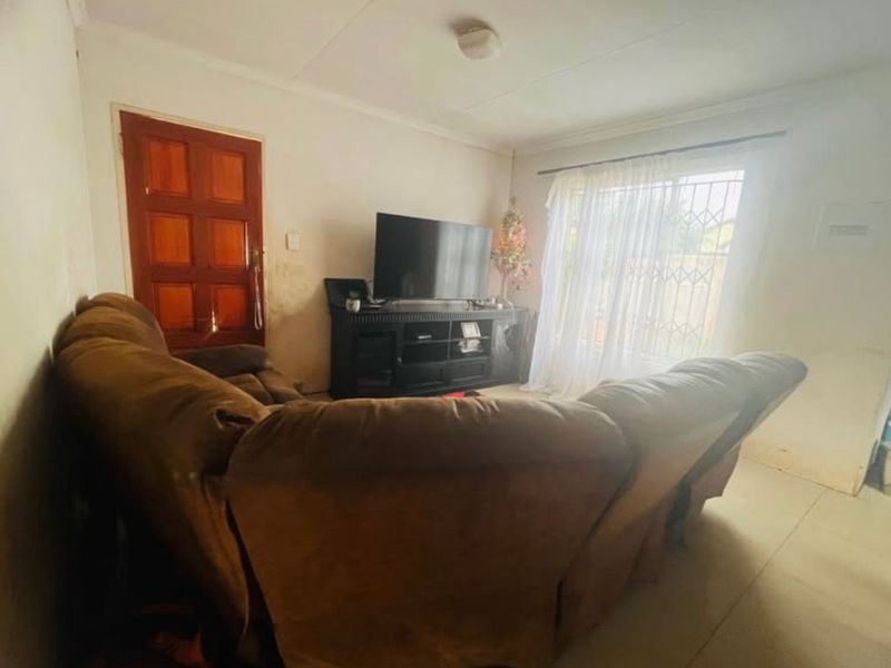 A living room featuring tiled flooring, a timber door, and a security gate, currently showing signs of wear on the walls.