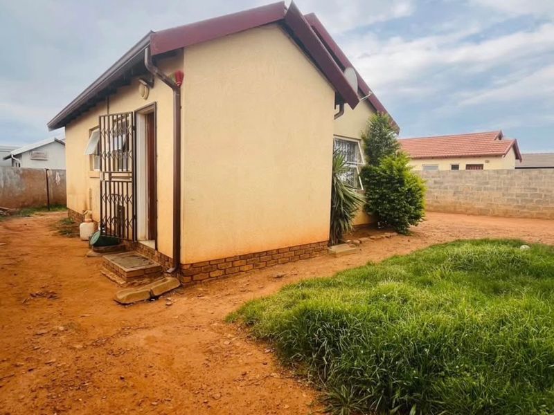 Rear view of a detached house featuring a pitched roof, metal security gate, and an unpaved yard area with a concrete boundary wall.