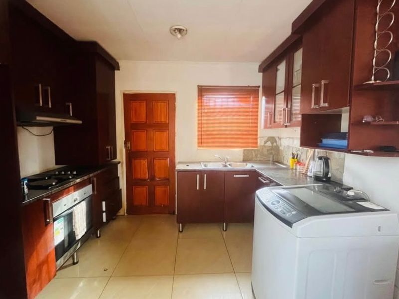 A functional kitchen featuring dark wood cabinetry, granite countertops, built-in oven and hob, and tiled flooring with direct access to an exterior door.
