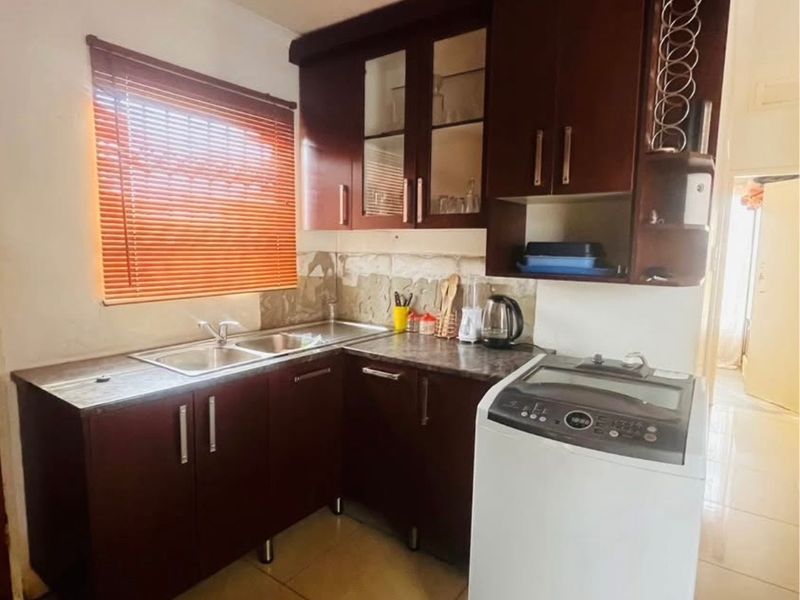 Compact kitchen featuring dark wood cabinetry, laminate countertops, and a double bowl stainless steel sink, with tiled flooring throughout.