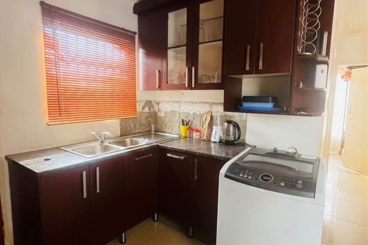 Compact kitchen featuring dark wood cabinetry, laminate countertops, and a double bowl stainless steel sink, with tiled flooring throughout.