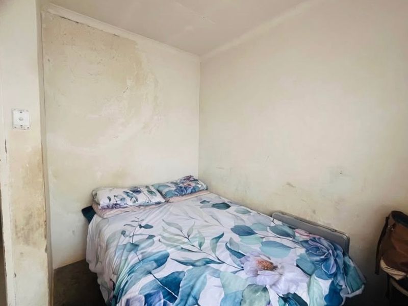 A bedroom space requiring maintenance, featuring visible wall staining and signs of potential moisture damage on the interior surfaces.