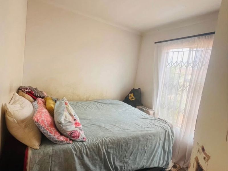 A bedroom featuring a window with a security gate and curtain rod, showing visible wall damage and staining requiring maintenance and cosmetic repair.