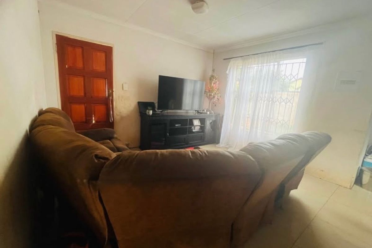 A living room featuring tiled flooring, a timber door, and a security gate, currently showing signs of wear on the walls.