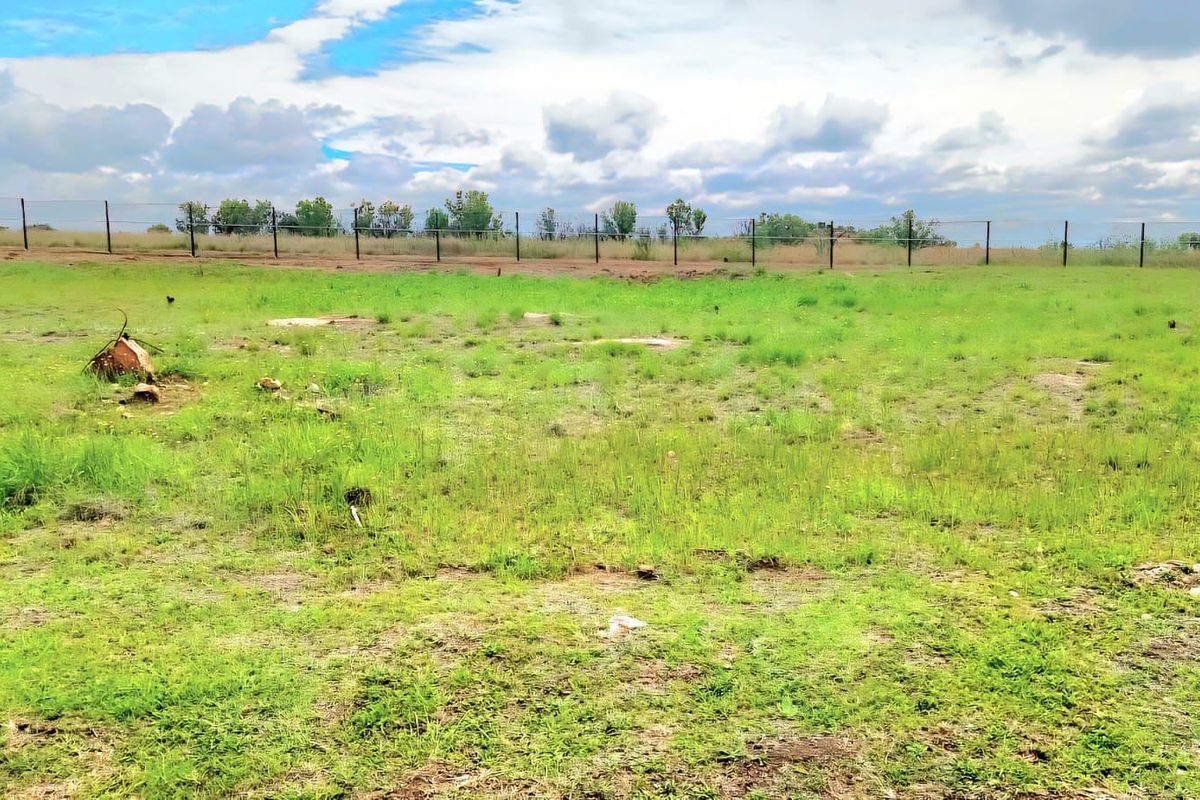 A vacant residential plot featuring open grassy terrain, enclosed by wire mesh perimeter fencing and equipped with a solar light pole.