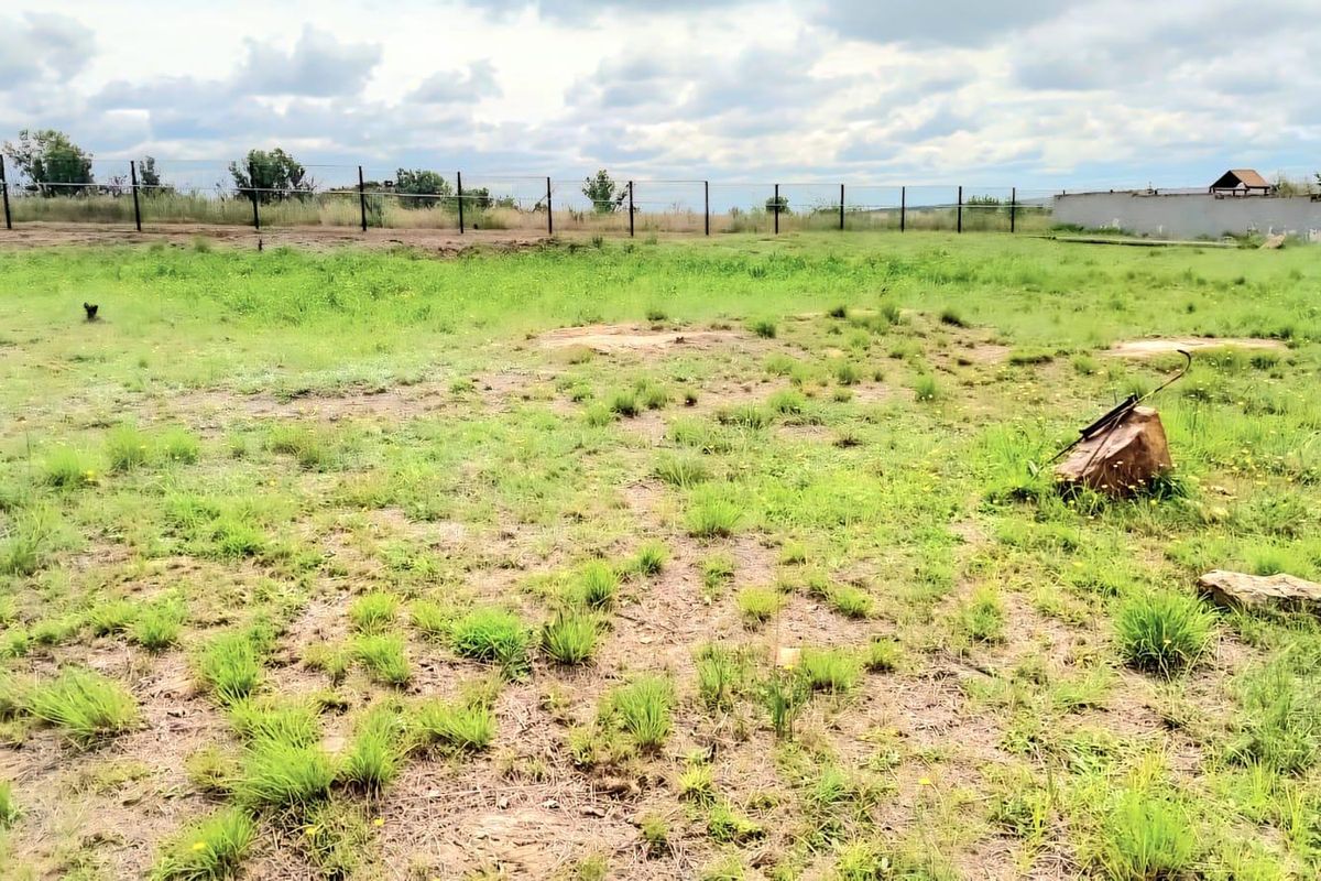 A view of a vacant residential plot featuring open grass land, perimeter fencing, and a boundary wall.