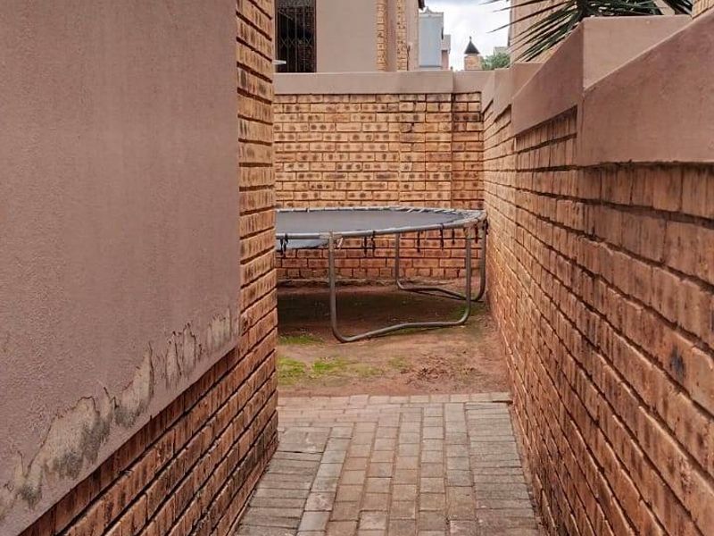A narrow side passage featuring brick paving and face brick boundary walls, showing signs of exterior wall plaster deterioration.
