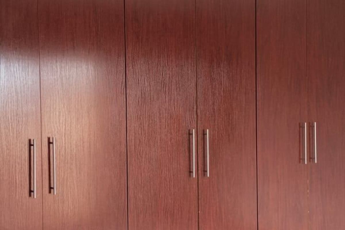 A bedroom featuring floor-to-ceiling built-in wooden cupboards with modern handles, providing ample storage space.