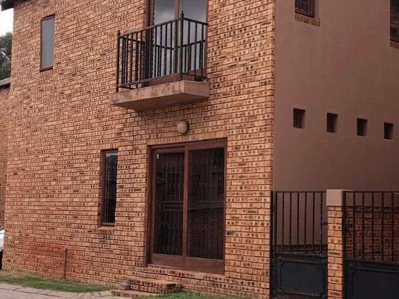 A two-story townhouse exterior featuring face brick construction, a small balcony with iron railing, and a paved driveway entrance.