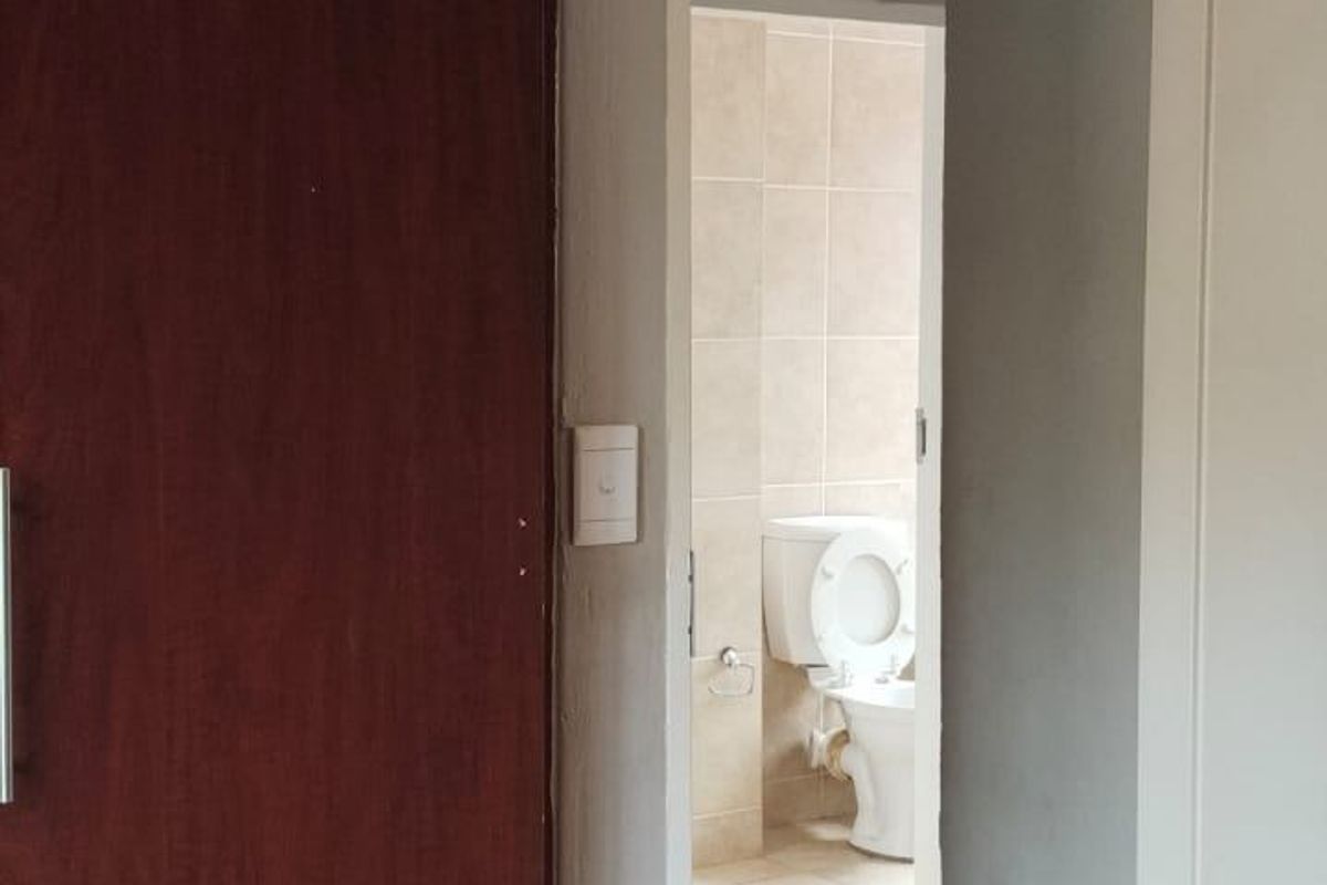 A view through a doorway into a bathroom featuring tiled flooring and walls, with a built-in cupboard visible in the adjacent room.