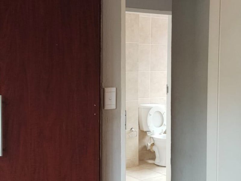 A view through a doorway into a bathroom featuring tiled flooring and walls, with a built-in cupboard visible in the adjacent room.