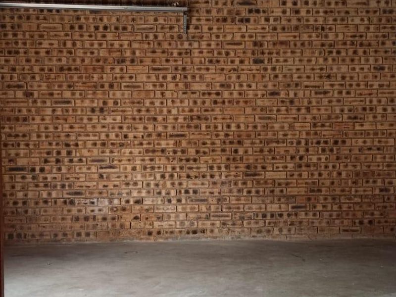 A functional, empty garage space featuring exposed brick walls, concrete flooring, and an automated door mechanism with visible ceiling rafters.
