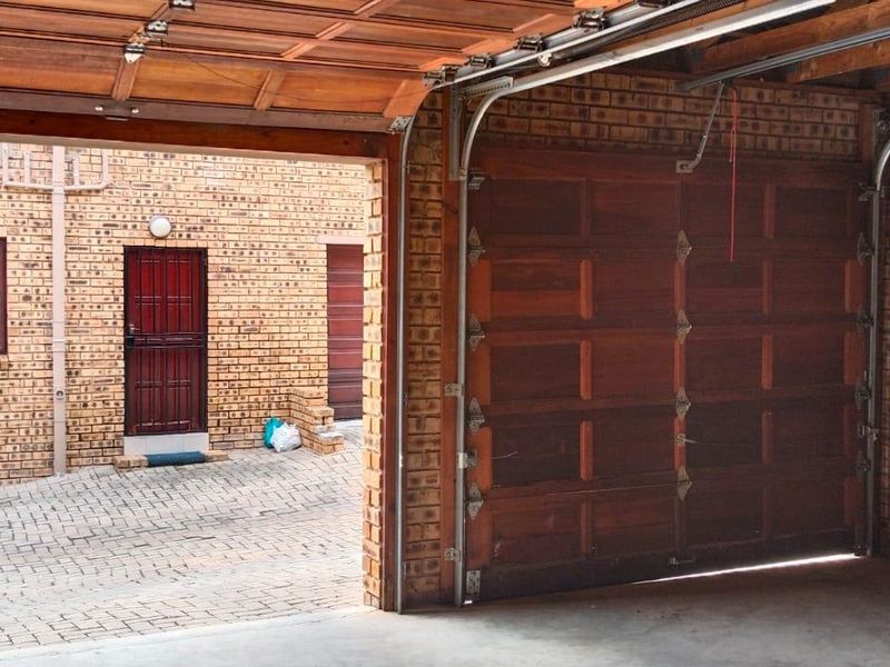 A spacious garage featuring exposed brick walls, concrete flooring, and a timber sectional door, opening onto a paved driveway area.