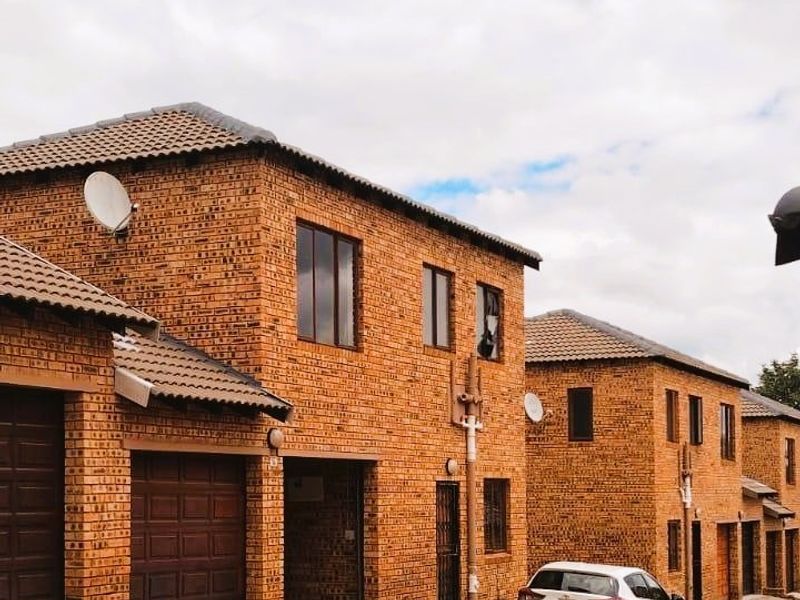 Exterior view of a multi-story townhouse complex featuring face brick construction, tiled roofing, and paved driveway access.