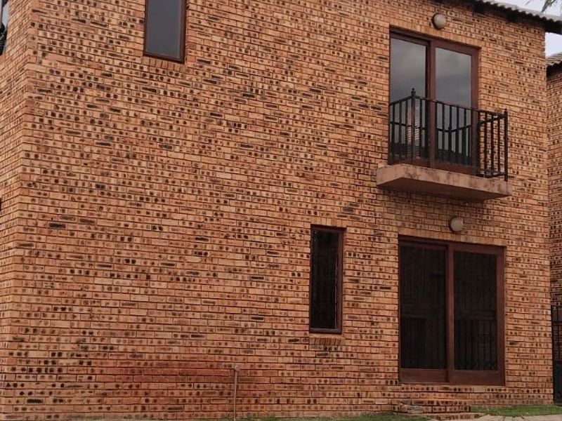 A two-story townhouse exterior featuring face brick construction, a small balcony with wrought iron railing, and a paved driveway area.