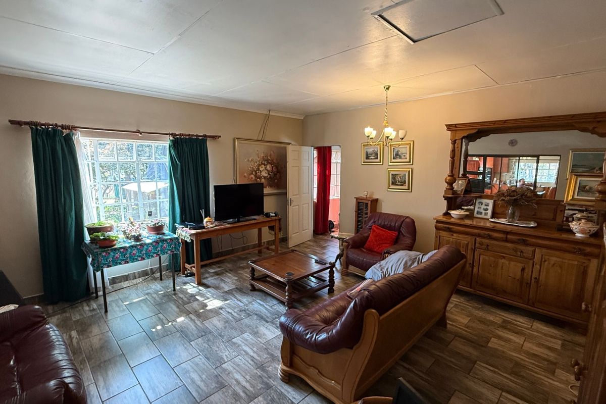 A spacious living room featuring tiled flooring, a central chandelier, and a large multi-pane window allowing natural light into the area.
