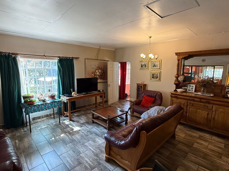 A spacious living room featuring tiled flooring, a central chandelier, and a large multi-pane window allowing natural light into the area.