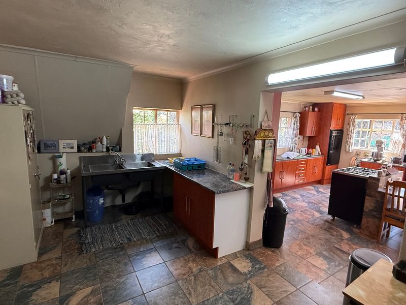 Open plan kitchen and scullery area featuring stone-look tile flooring, laminate cabinetry, and integrated cooking appliances in need of modernization.