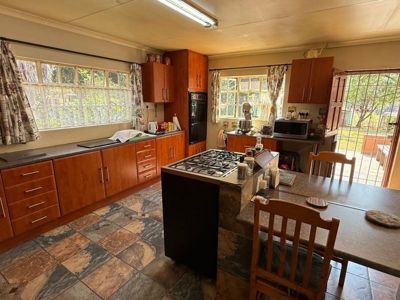 A functional kitchen featuring wooden cabinetry, a central gas hob, tiled flooring, and direct access to the rear exterior through a security gate.