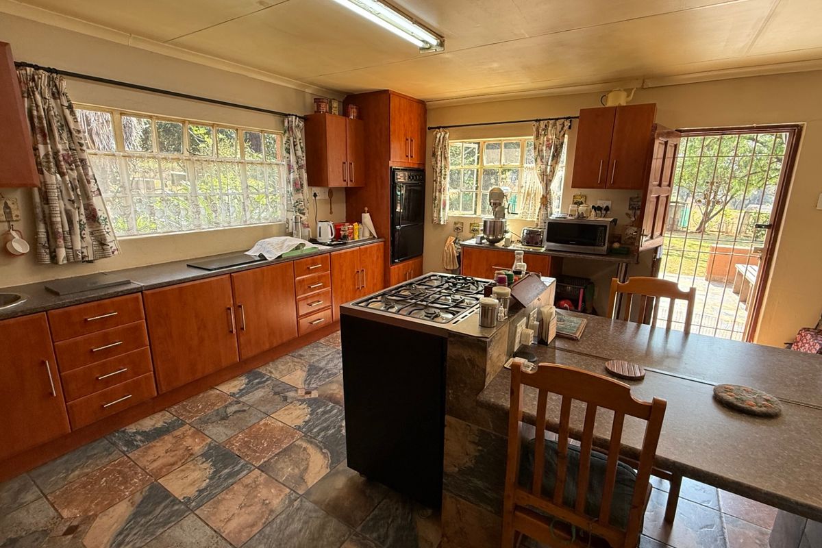 A functional kitchen featuring wooden cabinetry, a central gas hob, tiled flooring, and direct access to the rear exterior through a security gate.