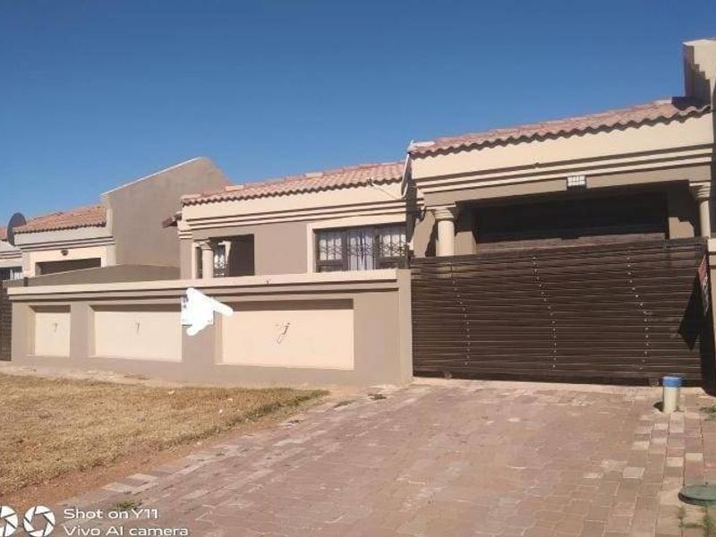 Front elevation of a residential property featuring a paved driveway, perimeter wall, and a large sliding gate.